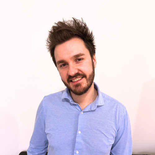 white man smiling in a white background, wearing a blue shirt